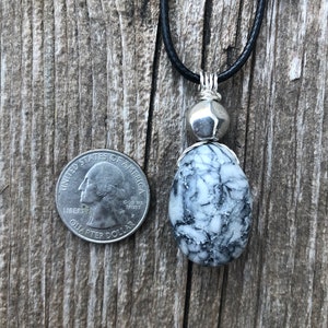 May include: A black leather cord necklace with a silver pendant featuring a white and black marbled stone. The stone is about the size of a UK 20 pence coin.
