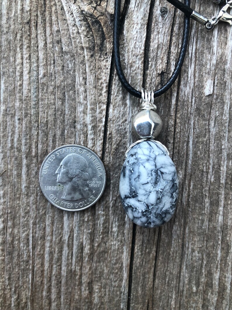May include: A black leather cord necklace with a silver pendant featuring a white and black marbled stone. The stone is about the size of a UK 20 pence coin.