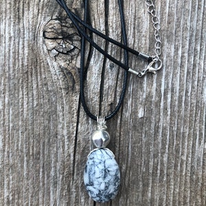 May include: A black cord necklace with a silver pendant featuring a white and grey oval stone.