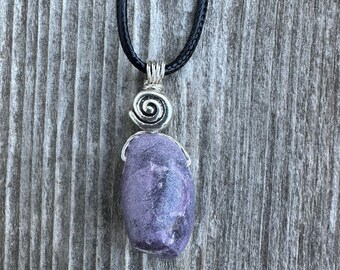 May include: A purple stone pendant necklace with a silver swirl design. The necklace is on a black cord.
