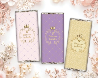 Könnte beinhalten: Drei Schokoriegel mit dekorativen Verpackungen. Jede Verpackung zeigt eine Krone, die Zahl 8 und die Worte "Princess Isabella". Die Verpackungen sind in Hellrosa, Lila und Gelb gehalten und haben ein Rautenmuster.