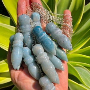 May include: A collection of blue and white crystal pendulums with silver chains. The pendulums are in the shape of a teardrop and have a pointed tip. They are held in a hand.