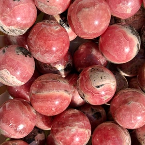K&ouml;nnte beinhalten: Eine Sammlung von rosa und schwarz gestreiften Kugeln aus poliertem Edelstein. Die Kugeln sind glatt und gl&auml;nzend, mit einer Vielzahl von Mustern und Texturen.