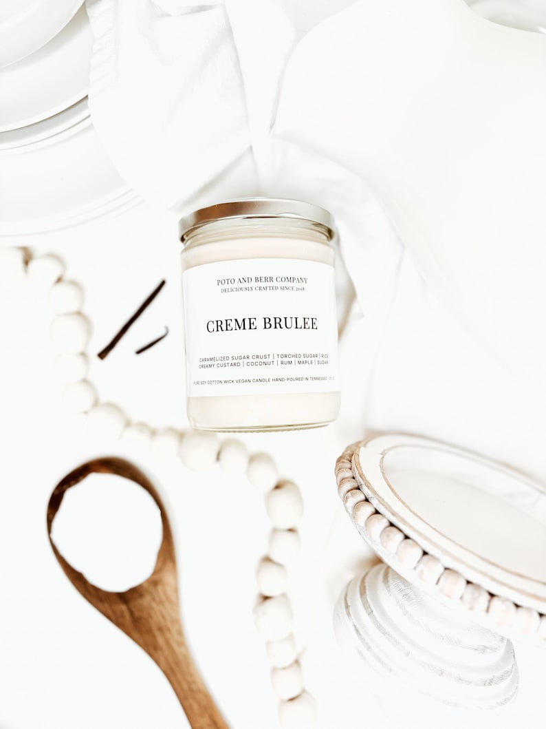 May include: A clear glass candle jar with a silver lid and a white label reading Poto and Berr Company, Creme Brulee, and a list of scent notes including caramelized sugar crust, torched sugar, creamy custard, coconut, rum, maple, and sugar.