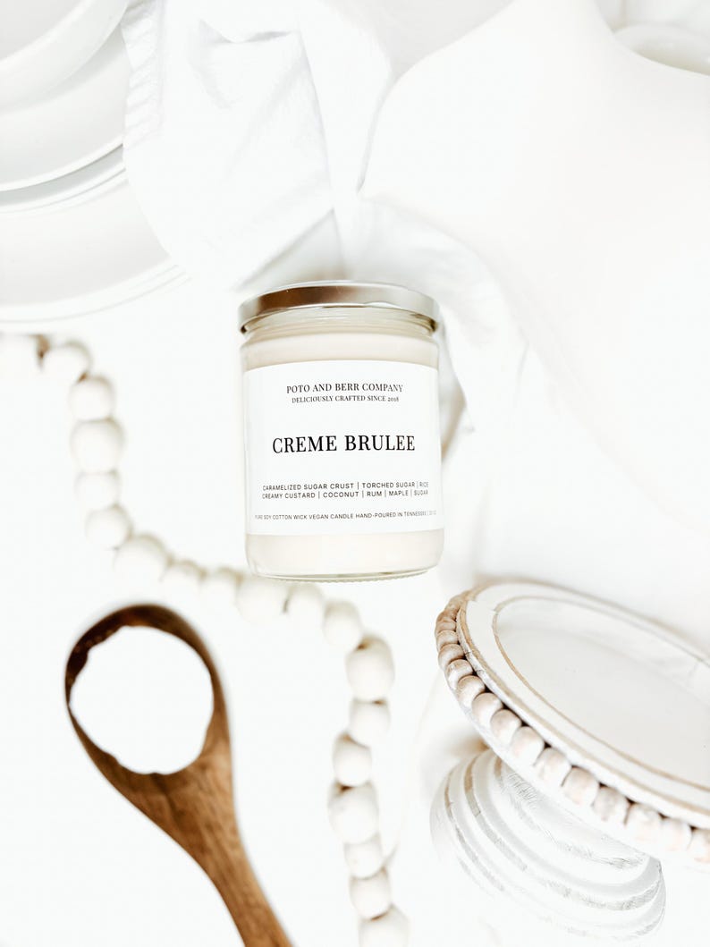 May include: A clear glass candle jar with a silver lid and a white label featuring the text Poto and Berr Company, Creme Brulee, and a list of scent notes including caramelized sugar crust, torched sugar, creamy custard, coconut, rum, and maple.