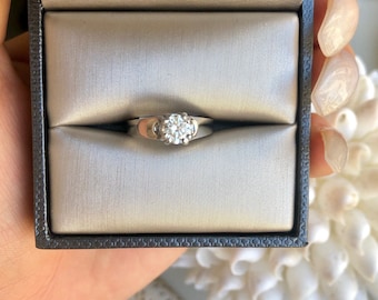 May include: A silver engagement ring with a round, clear diamond in a ring box.