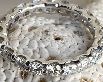 May include: A silver eternity band with a row of round diamonds set in a bezel setting.