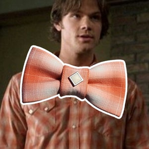 May include: Orange and white plaid bow tie with a square, silver-toned center detail. The bow tie is a classic accessory, perfect for adding a touch of style to any outfit. The plaid pattern adds a touch of visual interest.