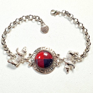 Puede incluir: Un brazalete de cadena de plata con un dije de tartán rojo y negro, un dije de oso y un dije de zorro.