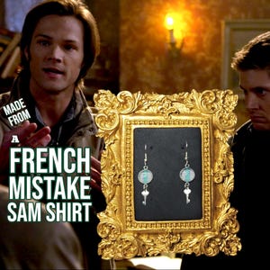 May include: A pair of silver earrings with a turquoise and white patterned charm and a silver key charm hanging from each earring. The earrings are displayed in a gold frame.