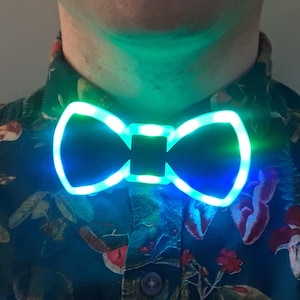 Op de afbeelding: Een zwarte strik met een lichtblauwe en groene LED-lichtcontour. De strik wordt gedragen door een persoon met een geprint overhemd.