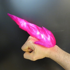May include: A pink, translucent, flame-shaped object, resembling a prop for a superhero costume, is worn on a person's hand.