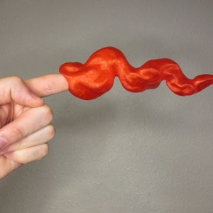 Peut inclure: Une main tenant un objet flexible et ondulé de couleur rouge vif qui ressemble à une flamme.