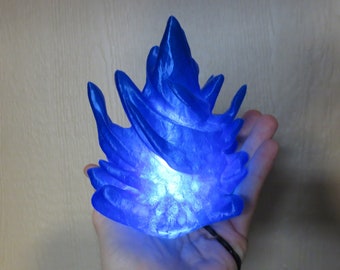 May include: A blue 3D printed flame sculpture with a glowing light inside. The flame is a stylized representation of fire with a jagged, pointed shape.