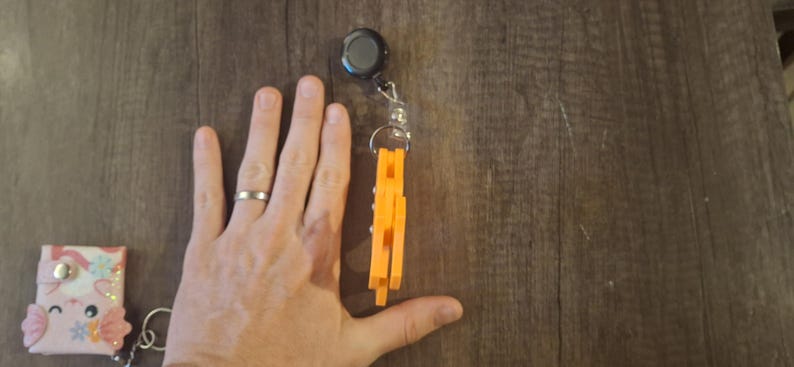 May include: An orange retractable badge holder with a black top and a silver chain. A small, pink and white card holder with a cartoon design is also visible. The items are on a wooden surface.