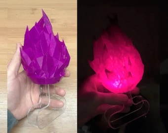 May include: A purple 3D printed crystal flame sculpture with a clear plastic base. The sculpture is lit from within, casting a warm glow.
