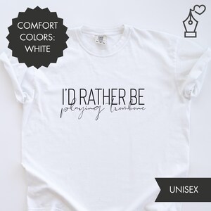 Op de afbeelding: Wit unisex T-shirt met de zwarte tekst "I'D RATHER BE playing trombone". Het shirt heeft ook de tekst "COMFORT COLORS: WHITE" in een zwarte cirkel en het woord "UNISEX" in een zwart rechthoek.