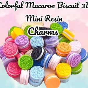 May include: A collection of colorful, 3D resin charms resembling macarons and sandwich cookies. The charms feature various colors like pink, purple, green, and blue, with the text "OREO" visible on some. The image includes the text "Colorful Macaron Biscuit 3D" and "Mini Resin Charms."