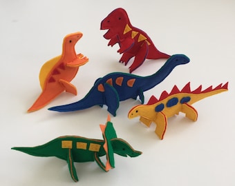 May include: A collection of colorful felt dinosaur toys in various shapes and sizes. The dinosaurs are in shades of red, orange, yellow, blue, and green, with contrasting details. The toys are handmade and suitable for children.