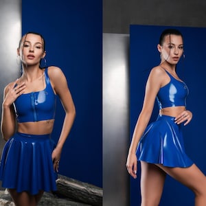 May include: A two-piece set consisting of a glossy royal blue sleeveless crop top with a front zipper closure and a matching high-waisted flared mini skirt. The material has a smooth, reflective finish and a vibrant, solid blue color throughout.