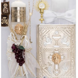 May include: First Communion set with a white candle, a gold chalice, a white bow tie, a rosary, a white and gold prayer book, and a white and gold decorative pillow.
