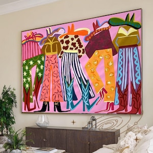 May include: Large framed abstract painting featuring stylized figures in cowboy boots and hats. The figures wear colorful patterned pants in pink, green, orange, and blue. The background is a solid pink, and the painting is signed "MEISHENGART since 2019".