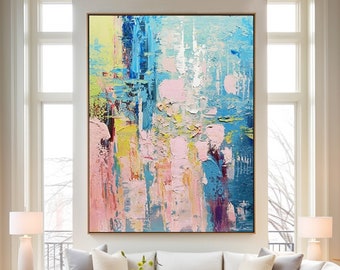 May include: Abstract painting with a mix of pink, blue, yellow, and white paint. The painting has a textured look and is framed in a simple, modern frame.