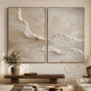 Puede incluir: Dos piezas de arte mural rectangulares grandes con una textura de empaste gruesa en blanco y beige. Las pinturas abstractas muestran pinceladas en relieve y superpuestas que crean un efecto de paisaje. Las obras están enmarcadas con bordes finos.