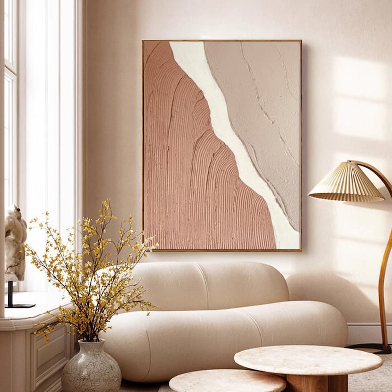 May include: Abstract painting with a textured, pink and white design. The painting is framed in a thin, gold frame and hangs on a light pink wall.