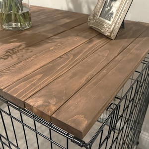 Peut inclure: Une table en bois avec une finition marron fonc&eacute; repose sur une structure en fil de fer noir. Le plateau est compos&eacute; de plusieurs planches de bois. Une photo encadr&eacute;e d&eacute;corative et un vase en verre avec des fleurs sont sur le dessus.