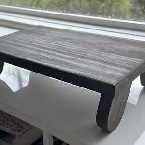 May include: A gray wooden stand with rounded legs. The stand is made of wood and has a natural grain pattern.
