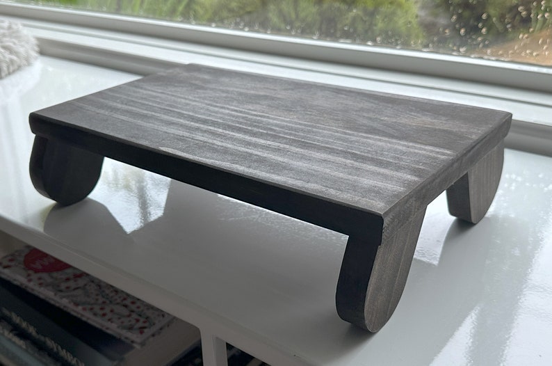 May include: A gray wooden stand with rounded legs. The stand is made of wood and has a natural grain pattern.