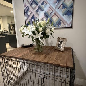 Peut inclure: Un enclos pour chien avec un dessus en bois, orn&eacute; d'un bouquet de fleurs blanches dans un vase en verre, d'une photo encadr&eacute;e et d'un bol noir. Une &oelig;uvre d'art g&eacute;om&eacute;trique est accroch&eacute;e au mur.