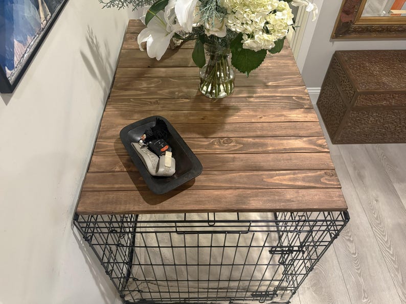 Peut inclure: Une caisse pour chien avec un plateau en bois brun fonc&eacute;. Un plateau noir avec divers objets est pos&eacute; sur le dessus, et un vase de fleurs blanches et de verdure est &eacute;galement pr&eacute;sent. La caisse a un cadre en fil de fer.