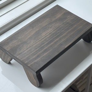 May include: A dark gray wooden stand with rounded legs. The stand is made of wood and has a natural grain pattern.