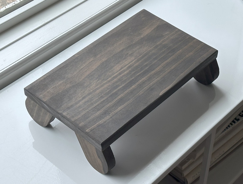 May include: A dark gray wooden stand with rounded legs. The stand is made of wood and has a natural grain pattern.