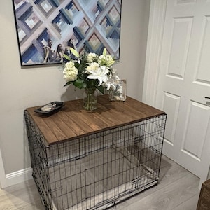 Peut inclure: Une cage pour chien en m&eacute;tal noir avec un dessus en bois, utilis&eacute;e comme table d'appoint. Le dessus est de couleur marron fonc&eacute;. Un vase de fleurs blanches et un plateau d&eacute;coratif sont pos&eacute;s dessus. Une peinture est accroch&eacute;e au mur derri&egrave;re la table.
