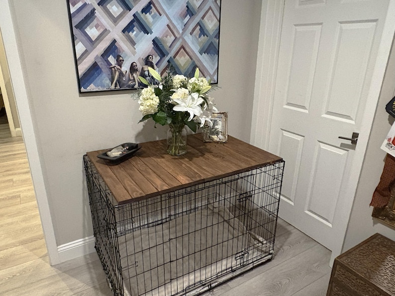Peut inclure: Une cage pour chien en m&eacute;tal noir avec un dessus en bois, utilis&eacute;e comme table d'appoint. Le dessus est de couleur marron fonc&eacute;. Un vase de fleurs blanches et un plateau d&eacute;coratif sont pos&eacute;s dessus. Une peinture est accroch&eacute;e au mur derri&egrave;re la table.