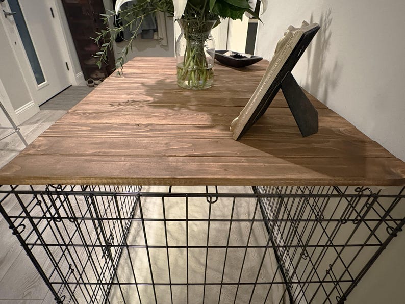 Peut inclure: Une cage pour chien rustique avec un dessus en bois. Le dessus est en bois teint&eacute; et de forme rectangulaire. La base de la cage est en fil de fer noir. Un cadre photo d&eacute;coratif et un vase avec des fleurs sont sur le dessus.