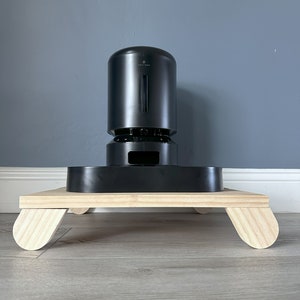 May include: A black pet feeder with a wooden base. The feeder has a round, cylindrical design and a small opening on the front. The base has four rounded legs.
