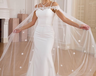 May include: A white wedding dress with a lace bodice and a tulle cape with pearl embellishments. The dress has a fitted bodice and a flowing skirt.