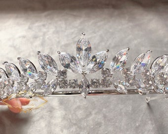 May include: A silver tiara with a row of marquise-shaped clear crystals, accented with smaller round crystals. The tiara has a delicate, feminine design.