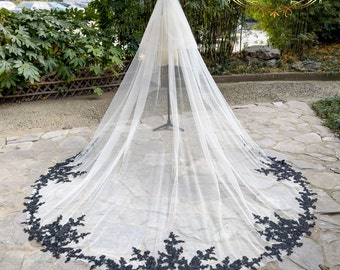 May include: A white bridal veil with a black lace trim. The veil is long and flowing, and the lace trim is delicate and intricate.