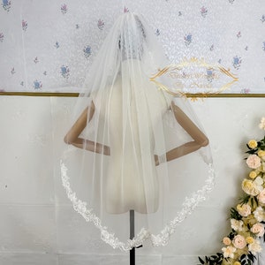 Puede incluir: Un velo de novia blanco con un delicado borde de encaje. El velo está hecho de tul suave y tiene una sola capa.