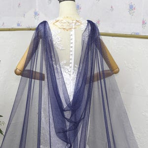 以下が含まれることがあります： シルバーのグリッターが付いたネイビーブルーのチュール製のウェディングケープ。ケープは透き通っており、流れるようなデザインです。