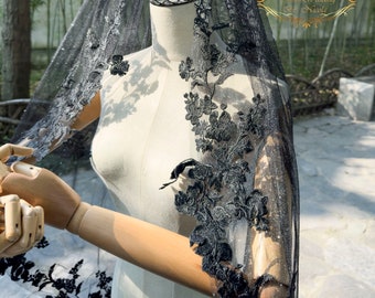 May include: A black wedding veil featuring a shimmering glitter finish and intricate black floral lace embroidery along the edges. The veil is draped over a mannequin and includes a gold logo graphic that reads Dream Wedding By Nicola.
