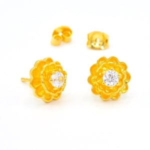 May include: A pair of gold flower-shaped earrings with a clear rhinestone in the center of each flower.