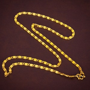 May include: A bright yellow gold chain necklace featuring a repeating pattern of interlocking oval links with a textured, swirling design. The necklace includes a secure S-hook clasp at one end and displays the text Best Thai Gold.