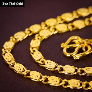May include: A bright yellow gold chain necklace featuring repeating S-shaped links and a secure hook clasp. The text Best Thai Gold is visible in the upper left corner and repeated in small print on the chain links and the clasp mechanism.