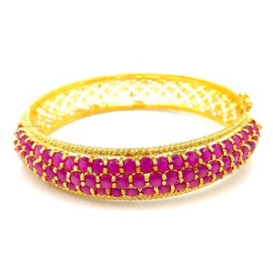 Puede incluir: Un brazalete de oro con un delicado diseño de filigrana y tres filas de piedras preciosas rosas.